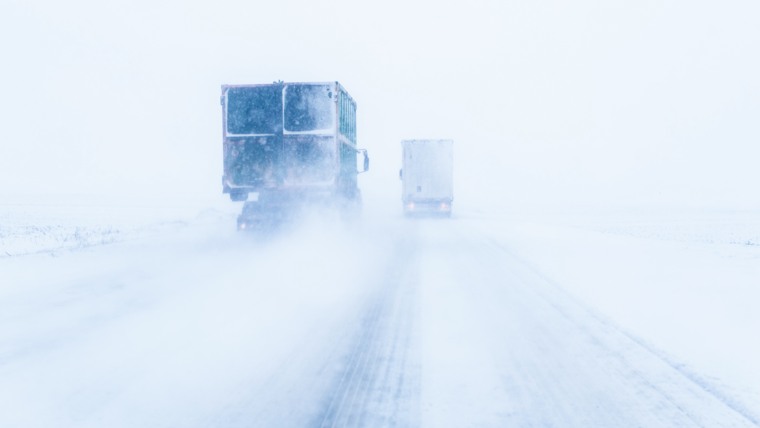 Två lastbilar kör på en väg i snöstorm