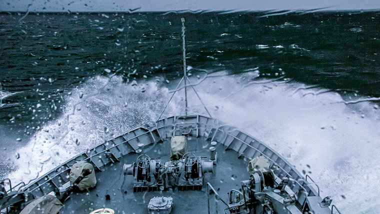 Militärskepp kör på öppet hav i vågstänk och regn.