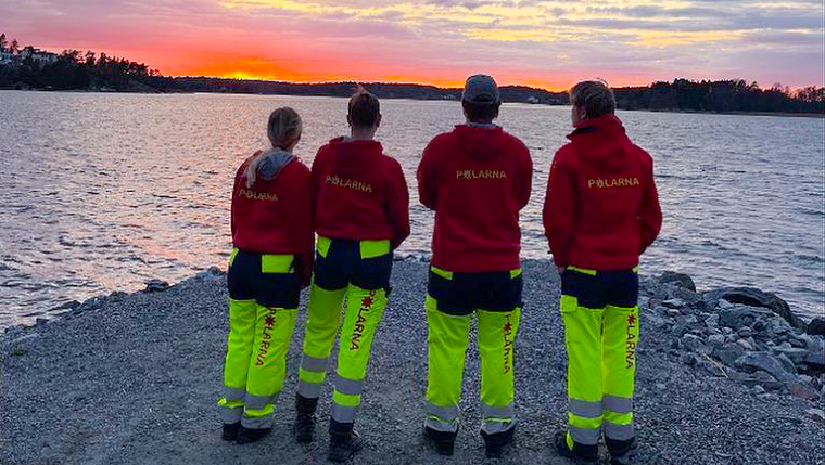 Fyra ungdomar tittar ut mot vattnet i solnedgången i kläder med texten "Polarna".