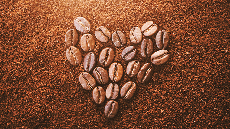 Kaffebönor ligger i formen av ett hjärta på malet kaffepulver.