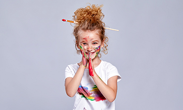 En flicka har en pensel uppsatt i håret och färg på sina händer.