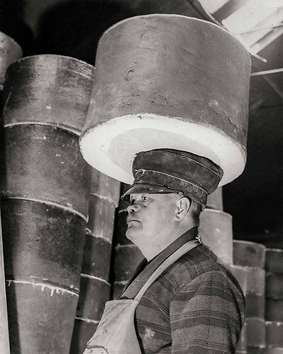 En man står med förkläde i fabriken och cylinderbehållare står bakom och åker i transport runt honom.